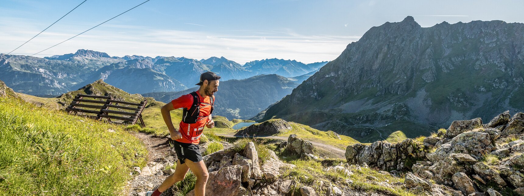 Ein Läufer in einem orangen T-Shirt läuft entlang dem Trail im Seetal | © Silvretta Montafon - Stefan Kothner