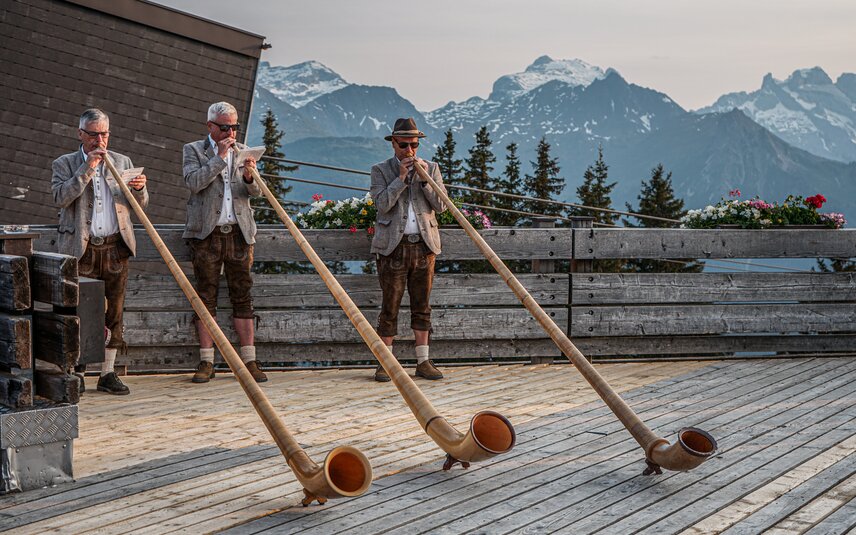 Drei Alphorngläser spielen auf einer Terrasse in den Bergen der Silvretta MOntafon. | © Silvretta Montafon - Vanessa Strauch