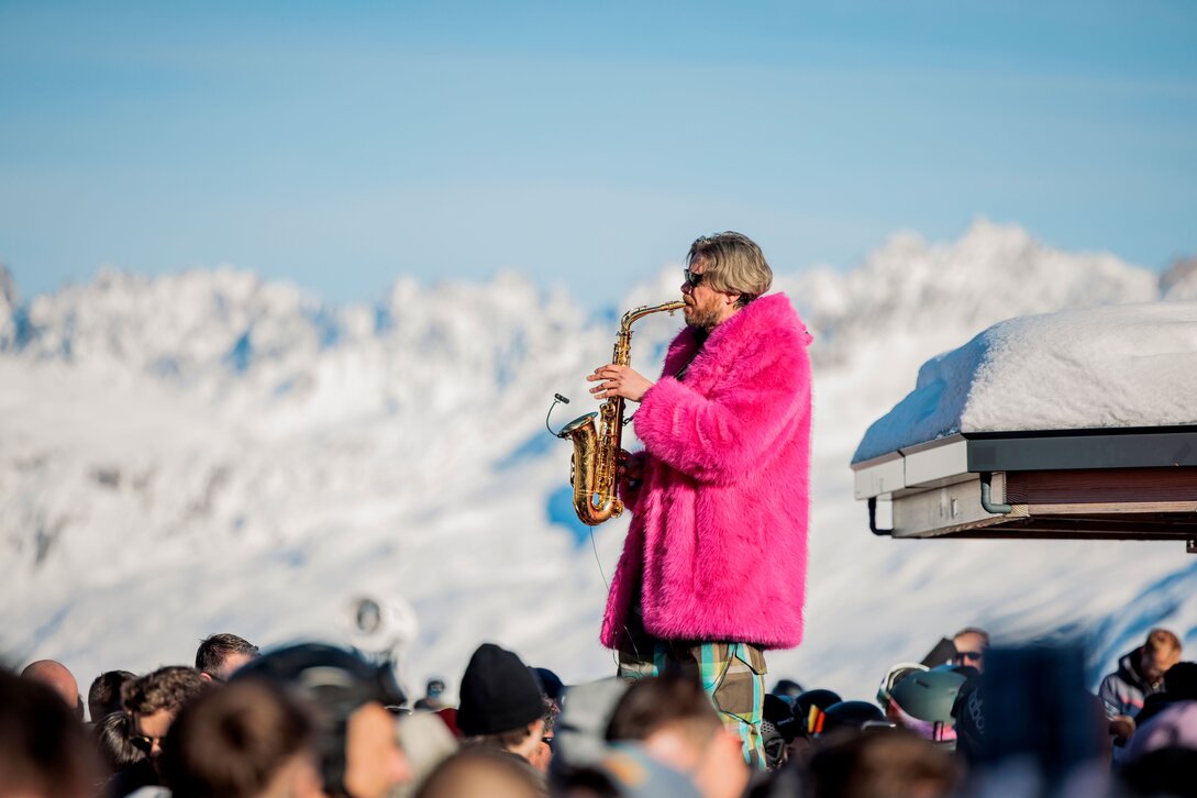 Saxophon-Spieler im pinken Fellmantel auf einer Bühne im Skigebiet Silvretta Montafon. | © Silvretta Montafon - Timmengerink