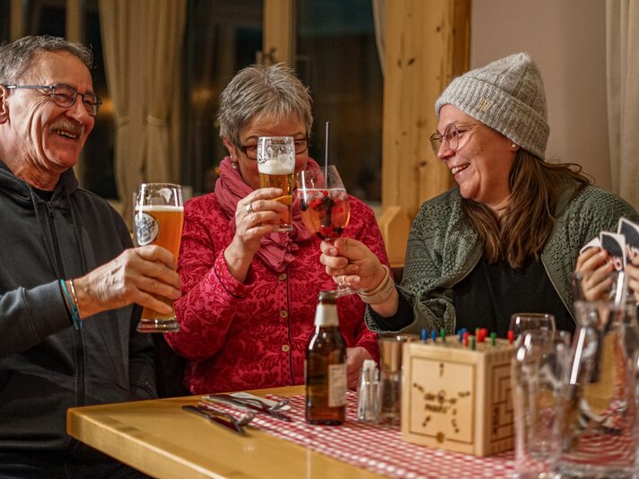 Drei Personen stoßen in einer gemütlichen Berghütte an. | © Vanessa Strauch - Silvretta Montafon