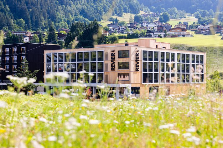 Eine grüne Wiese mit Blumen und im Hintergrund die Revier Mountain Lodge in der Silvretta Montafon. | ©   Silvretta Montafon | Revier Hotel Montafon