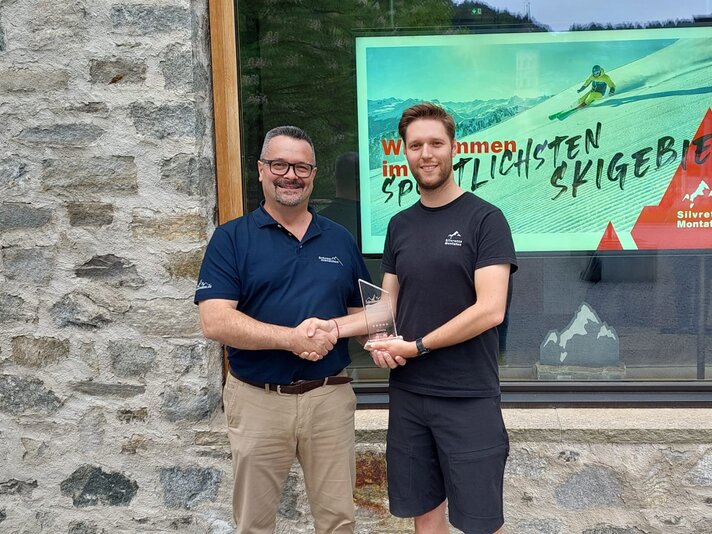Zwei Männer überreichen sich einen Award zum umweltschonenden Skigebiet vor der Alpin Sport Zentrale in Schruns | © Silvretta Montafon