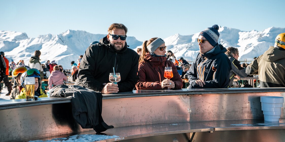 Drei Personen mit einem Getränk auf der Bella Nova Terrasse bei Sonnenschein. | © Silvretta Montafon - Vanessa Strauch