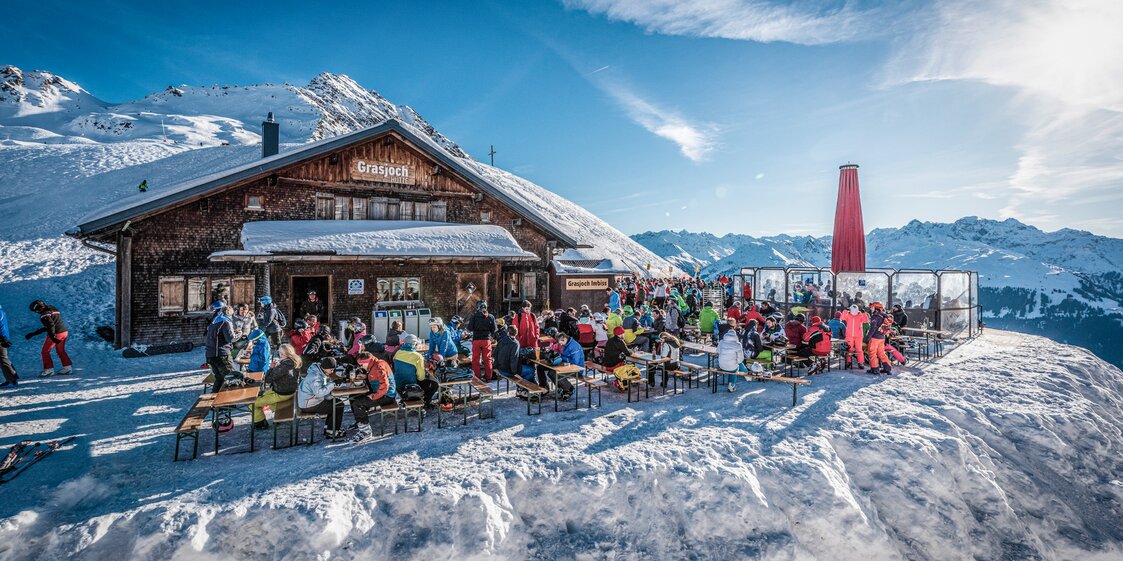 Die Grasjochhütte mit der gefüllten Terrasse bei schösten Winterwetter in der Silvretta Montafon. | © Silvretta Montafon - Marcel Mehrling