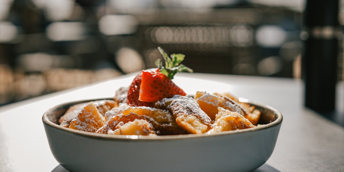 Ein Kaiserschmarren mit Erdbeere steht auf einem Tisch auf ener Terrasse in der Sonne. | © Silvretta Montafon - Vanessa Strauch