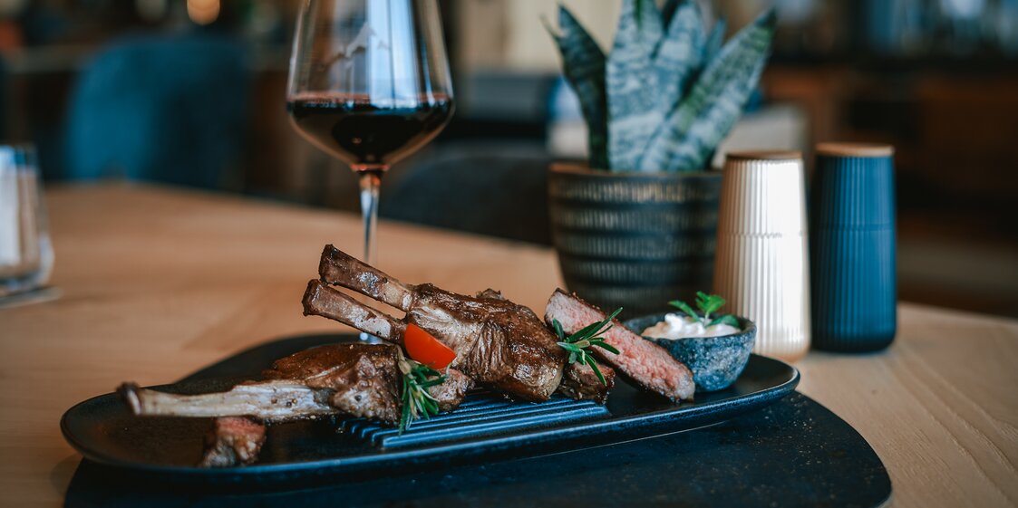 Lammracks auf einem Teller garbiert mit einem Glas Rotwein daneben. | © Silvretta Montafon - Vanessa Strauch