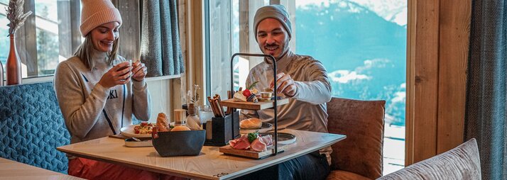 Eine Pärchen sitzt an einem gedeckten Tisch vor einem Bergpanorama im Winter. | © Silvretta Montafon - Vanessa Strauch