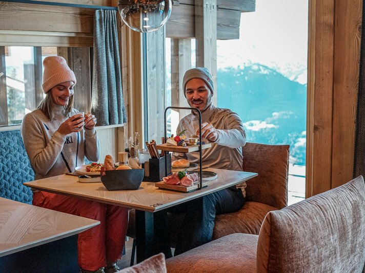 Eine Pärchen sitzt an einem gedeckten Tisch vor einem Bergpanorama im Winter. | © Silvretta Montafon - Vanessa Strauch