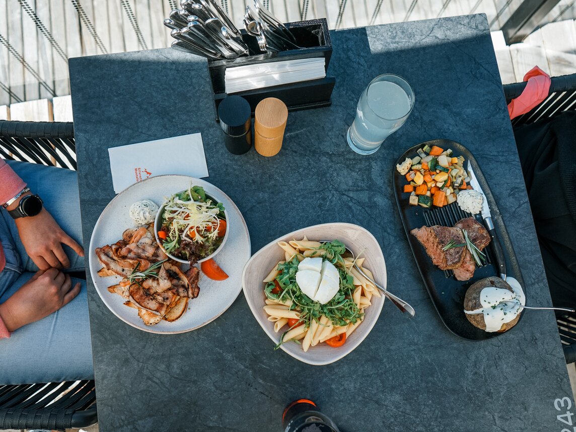 Ein gedeckter Tisch mit Nudelsalat, Ofenkartoffeln, Steal und Gemüse auf der Terrasse der Hanglage am Hochjoch in der Silvretta Montafon. | © Silvretta Montafon - Vanessa Strauch