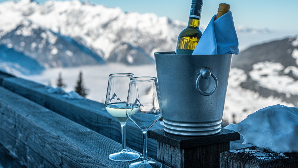 Zwei Weingläser und ein Weinkühler mit Wein stehen auf der Terrasse des Kapellrestaurants. | © Silvretta Montafon - Vanessa Strauch