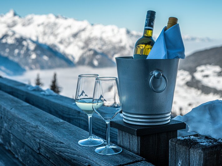 Zwei Weingläser und ein Weinkühler mit Wein stehen auf der Terrasse des Kapellrestaurants. | © Silvretta Montafon - Vanessa Strauch