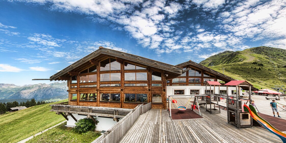 Die Aussenansicht des Kapellrestaurants im Sommer mit Spielplatz auf der Terrasse. | © Silvretta Montafon - Stefan Kothner