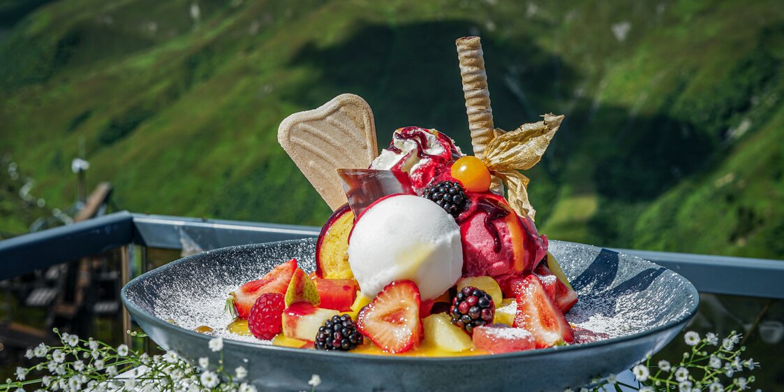 Ein Eis auf dem Teller mit verschiedenen Früchten und Bergen im Hintergrund | © Silvretta Montafon - Vanessa Strauch