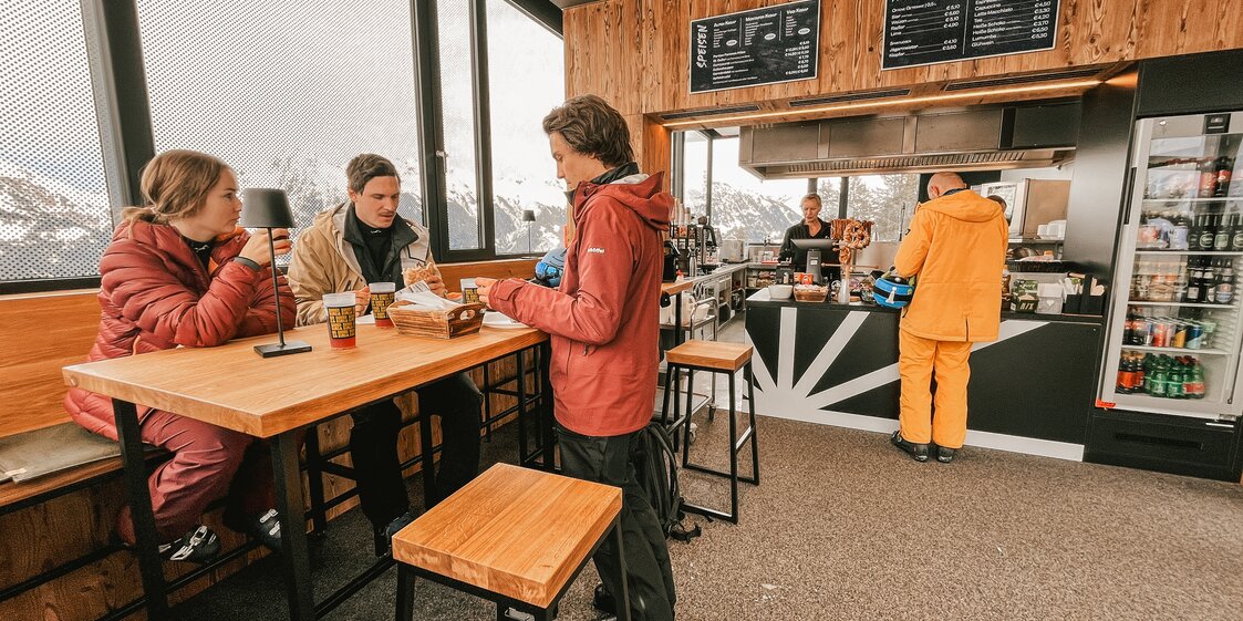 Drei Personen in der Sonnenbarga an einem Stehtisch und eine Person bestellt etwas an der Theke. | © Silvretta Montafon - Vanessa Strauch