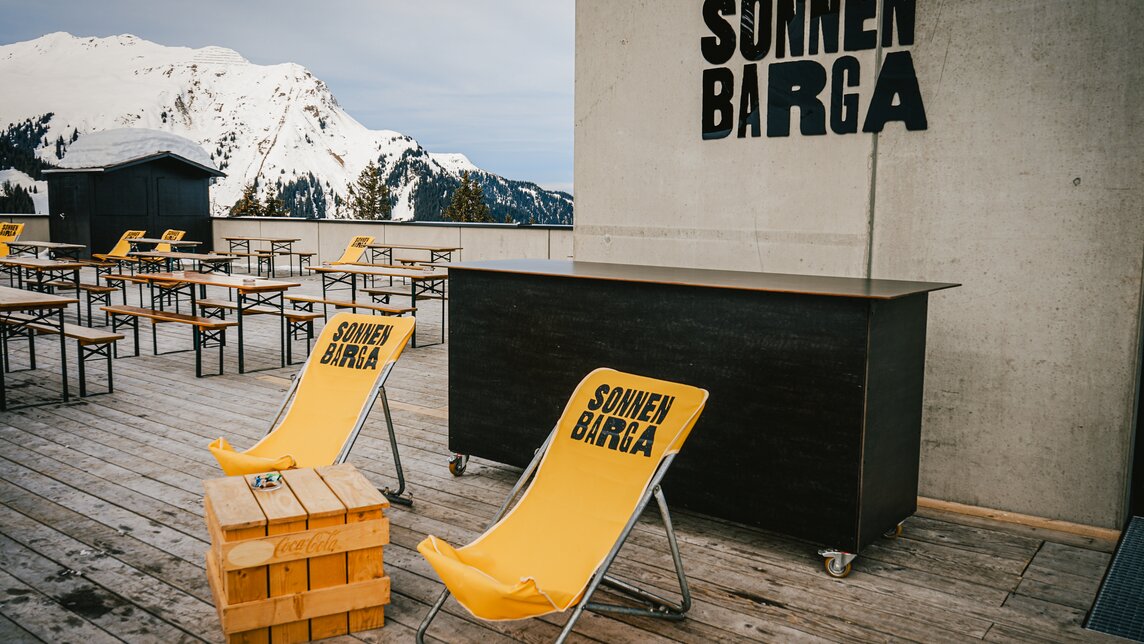 Der Eingang zur Sonnenbarga mit gelben Liegestühlen und Bierbänken auf der Terrasse. | © Silvretta Montafon - Vanessa Strauch