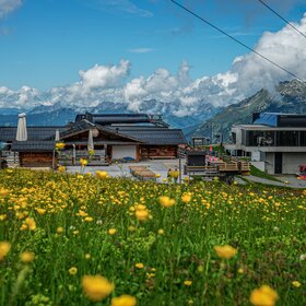 Das Valisera Hüsli von vorne mit der Bergstation der Valisera Bahn im Hintergrund | © Silvretta Montafon - Vanessa Strauch