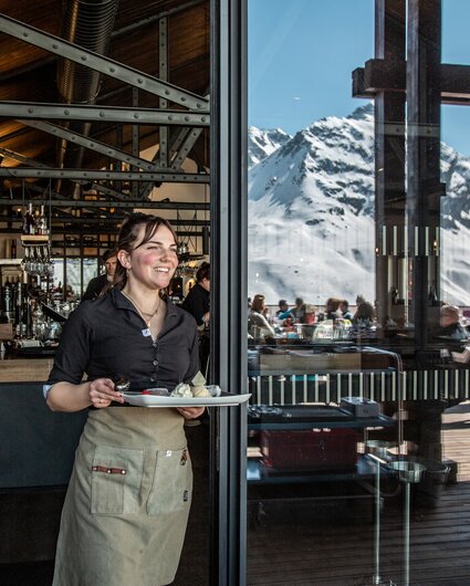 Eine Kellnerin bringt ein Dessert auf die Vinnova Terrasse. | © Silvretta Montafon - Friederike Weber