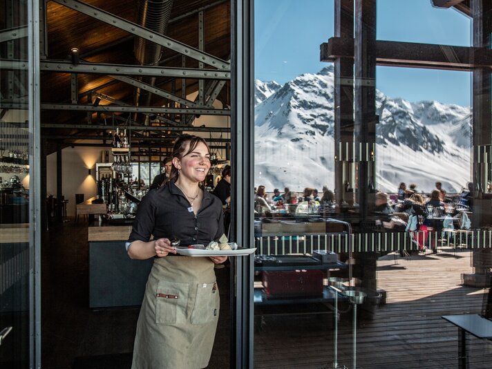 Eine Kellnerin bringt ein Dessert auf die Vinnova Terrasse. | © Silvretta Montafon - Friederike Weber