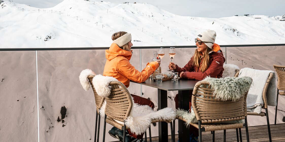 Zwei Frauen stoßen auf der Terrasse der Vinnova mit einem Glas Rosé Prosecco an. | © Silvretta Montafon - Vanessa Strauch