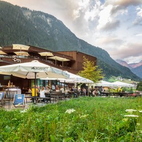  Ansicht des Restaurants von Aussen mit grüner Wiese im Vordergrund, Terrasse, Liegestühlen und Sonnenschirmen | © Silvretta Montafon - Stefan Kothner