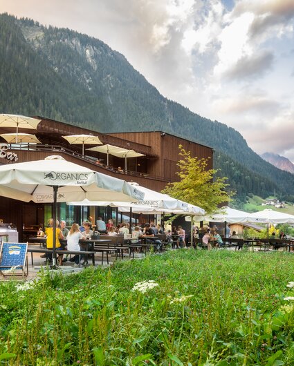  Ansicht des Restaurants von Aussen mit grüner Wiese im Vordergrund, Terrasse, Liegestühlen und Sonnenschirmen | © Silvretta Montafon - Stefan Kothner