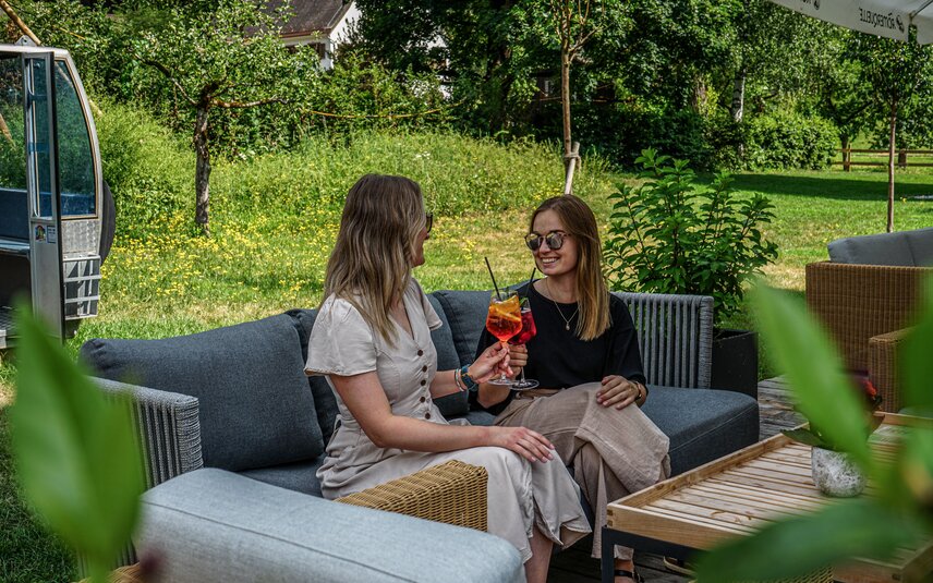Gemütliche Sitzecke mit zwei Frauen und einem erfrischenden Getränk auf der Josefsheim Terrasse. | © Silvretta Montafon - Vanessa Strauch