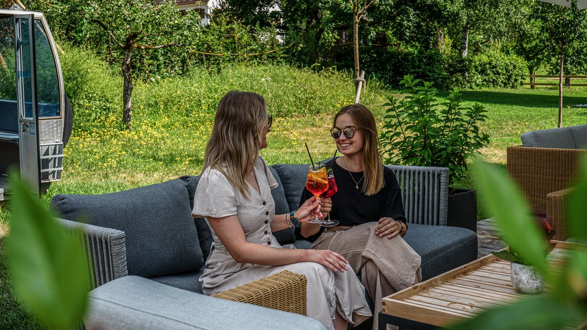 Gemütliche Sitzecke mit zwei Frauen und einem erfrischenden Getränk auf der Josefsheim Terrasse. | © Silvretta Montafon - Vanessa Strauch