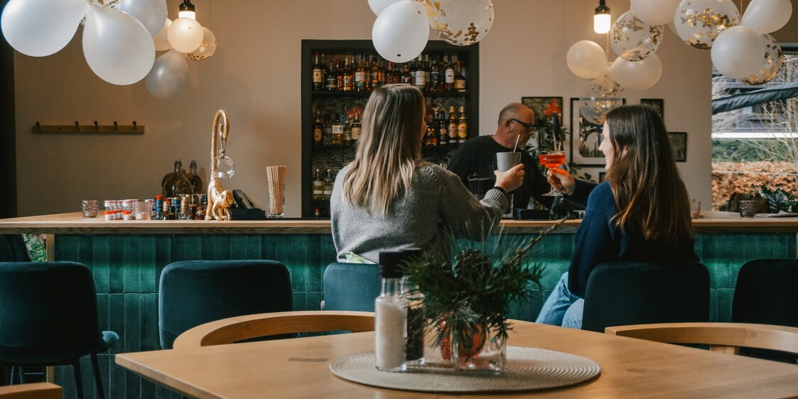 Zwei Frauen sitzen mit einem Drink an der Bar im Josefsheim Restaurant. | © Silvretta Montafon - Vanessa Strauch