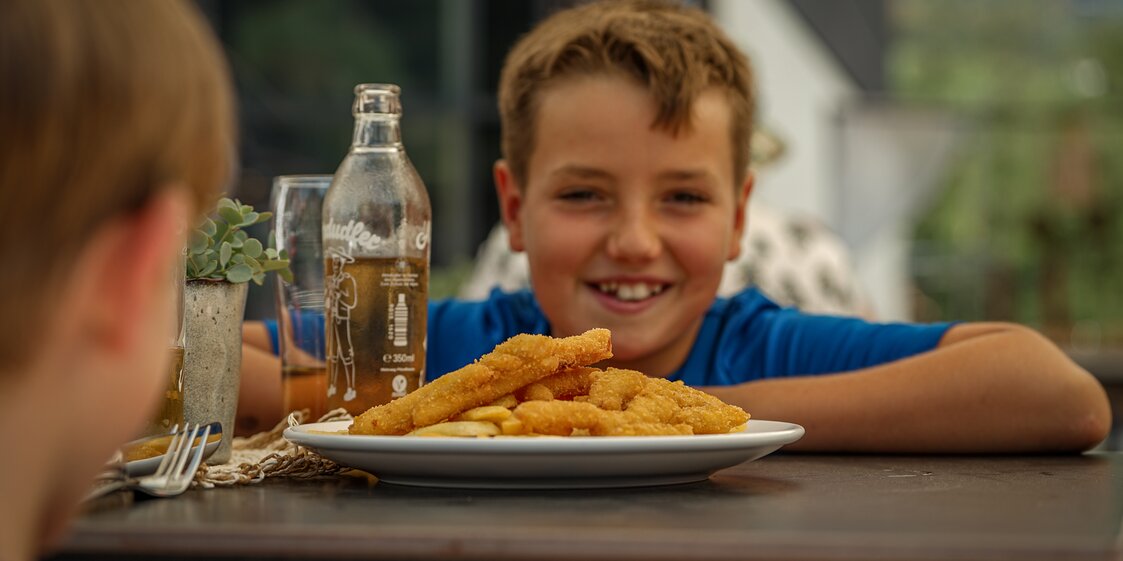 Kind freut sich über Chicken Fingers mit Pommes. | © Silvretta Montafon - Vanessa Strauch