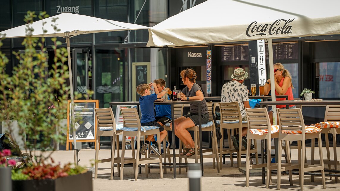 Personen sitzen an Tischen vor der Markthalle. | © Silvretta Montafon - Vanessa Strauch
