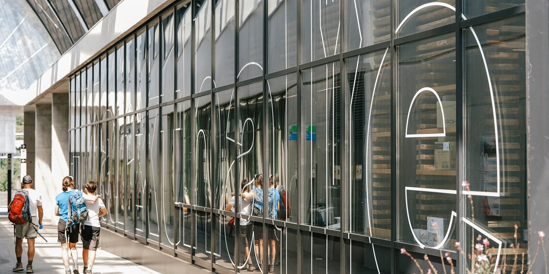 Drei Personen stehen vor einer Glasfassade auf der Markthalle geschrieben steht. | © Silvretta Montafon - Vanessa Strauch