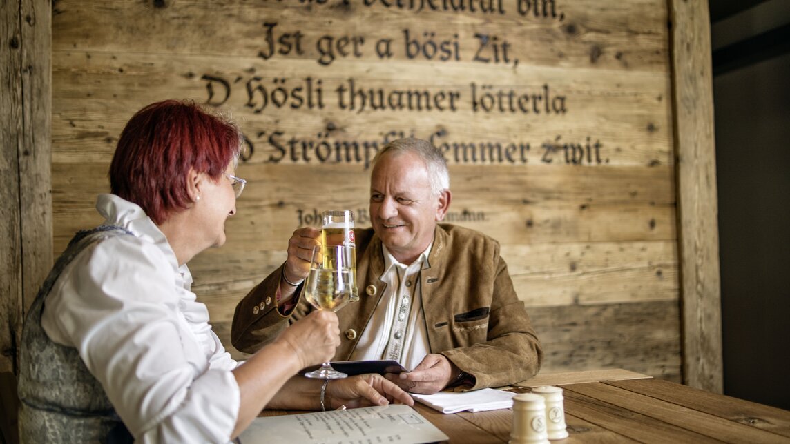 Ein älteres Ehepaar stößt mit Bier und Wein im Restaurant an. | © Silvretta Montafon - Markus Gmeiner