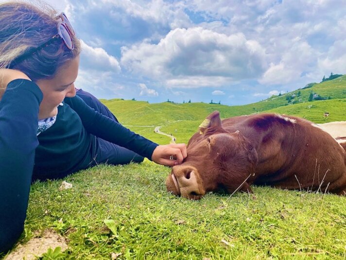 Ein Mädchen liegt auf einer Wiese in den Bergen und streichelt ein Kälbchen. | © Luisa Idler - Silvretta Montafon
