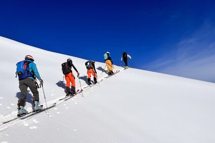 Gruppe von Freeridern beim Aufstieg im Tiefschnee bei blauem Himmel. | © Silvretta Montafon - Vanessa Strauch