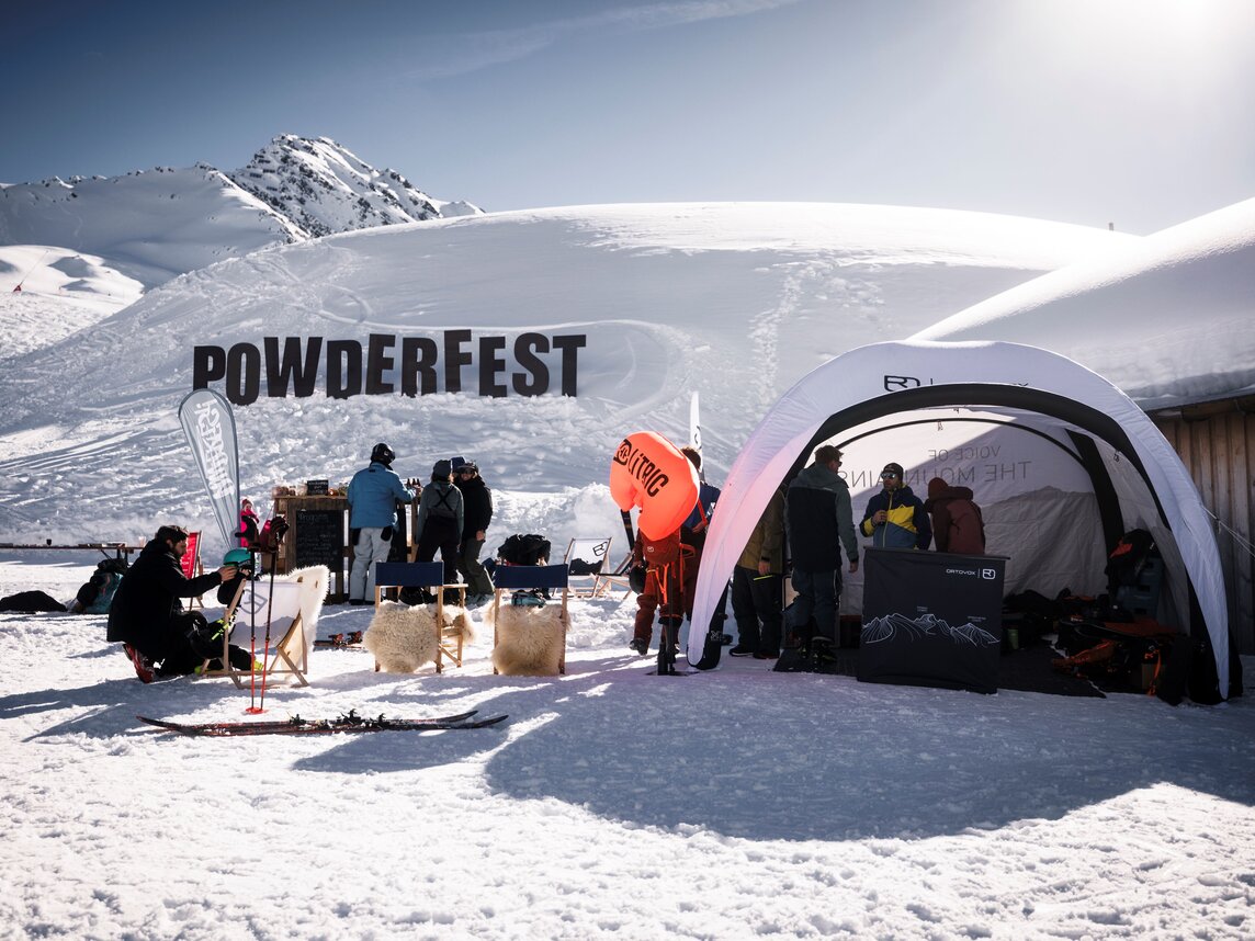 Der Schriftzug des Powderfestes im Schnee im Powderfest-Dorf mit Zelt und Liegestühlen. | © Max Dräger