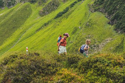 Eine Frau und ein Junge laufen zwischen grünen Wiesen in den Bergen. | © Silvretta Montafon - Roadtyping