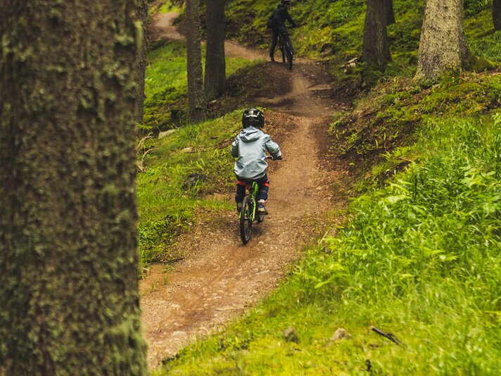 Ein Junge und eine erwachsene Person fahren auf einem Trailpark im Wald. | © Silvretta Montafon - Roadtyping