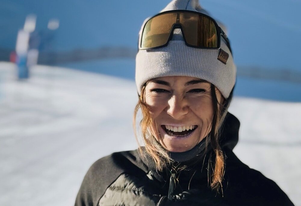 Eine Nahaufnahme mit einer lachenden Skilehrerin mit Mütze, Sonnenbrille, schwarzer Jacke und roter Skihose. | © Viola Schwigon - Silvretta Montafon