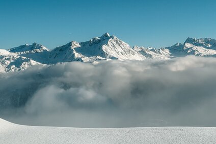 Verschneites Bergpanorama mit blauem Himmel und Nebel im Tal. | © Silvretta Montafon - Vanessa Strauch