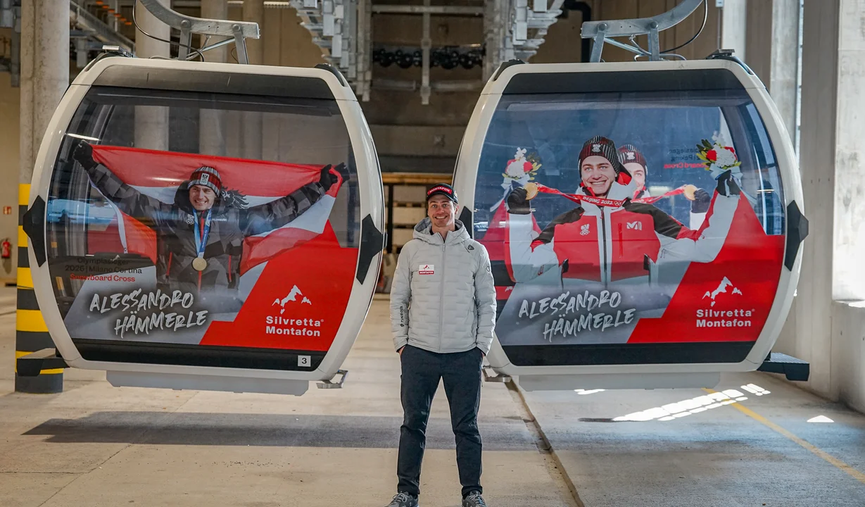Alessandro Hämmerle steht neben zwei gebrandeten Gondeln mit seinen Olympiasiegen | © Silvretta Montafon - Vanessa Strauch