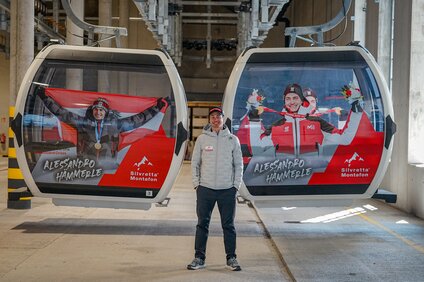 Alessandro Hämmerle steht neben zwei gebrandeten Gondeln mit seinen Olympiasiegen | © Silvretta Montafon - Vanessa Strauch