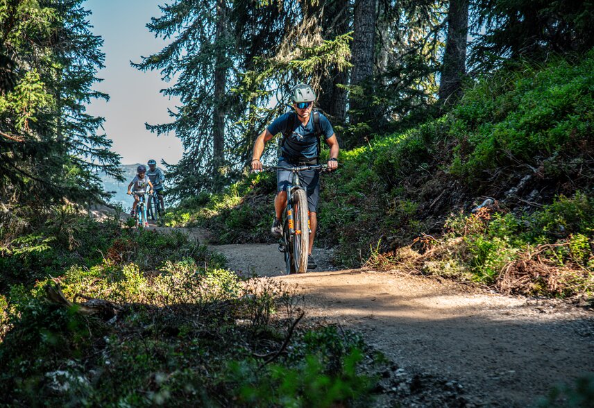 Ein Biker im Vordergrund und zwei Kinder im Hintergund fahren im Bikepark am Hochjoch in der Silvretta Montafon. | © Silvretta Montafon - Friederike Weber
