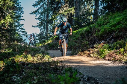 Ein Biker im Vordergrund und zwei Kinder im Hintergund fahren im Bikepark am Hochjoch in der Silvretta Montafon. | © Silvretta Montafon - Friederike Weber