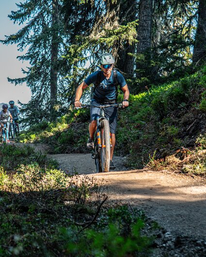 Ein Biker im Vordergrund und zwei Kinder im Hintergund fahren im Bikepark am Hochjoch in der Silvretta Montafon. | © Silvretta Montafon - Friederike Weber