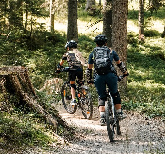 Eine Frau und ein Mädchen fahren auf einem Biketrail im Wald am Hochjoch in der Silvretta Montafon. | © Silvretta Montafon - Vanessa Strauch