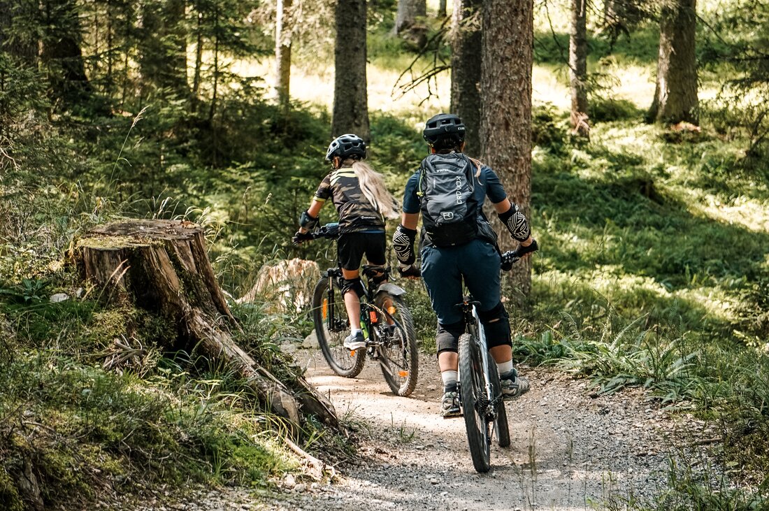 Eine Frau und ein Mädchen fahren auf einem Biketrail im Wald am Hochjoch in der Silvretta Montafon. | © Silvretta Montafon - Vanessa Strauch