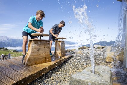 Vier Kinder an Wasserfontänen am Naturkräftepfad am Erlebnisberg Hochjoch in der Silvretta Montafon. | © Silvretta Montafon - Stefan Kothner