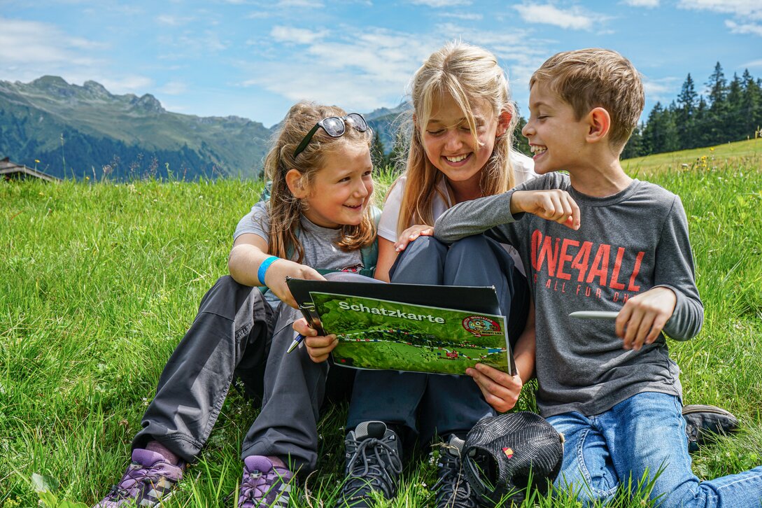 Drei Kinder sitzen in der Wiese bei der Schatzsuche auf Garfrescha in der Silvretta Montafon. | © Silvretta Montafon - Vanessa Strauch