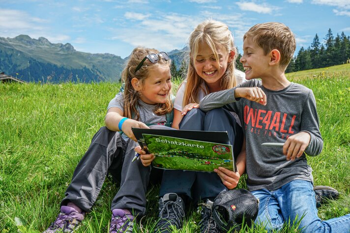 Drei Kinder sitzen in der Wiese bei der Schatzsuche auf Garfrescha in der Silvretta Montafon. | © Silvretta Montafon - Vanessa Strauch