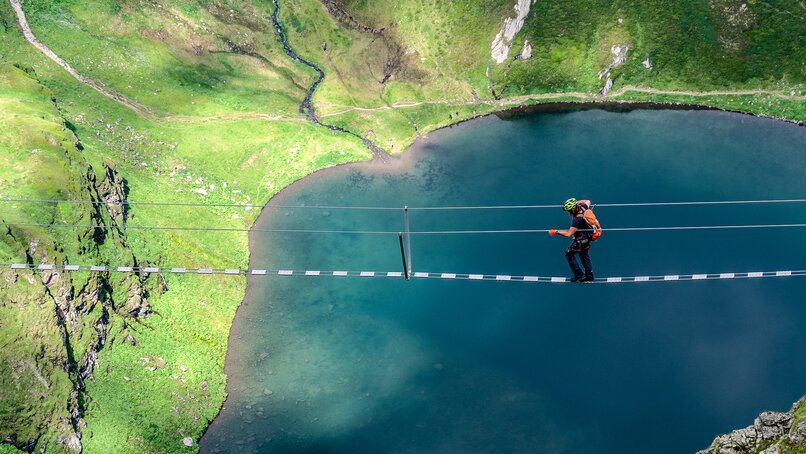 Ein Kletterer auf einer Seilbrücke oberhalb eines Bergsees in der Silvretta Montafon. | © Silvretta Montafon - Bertram Waldner